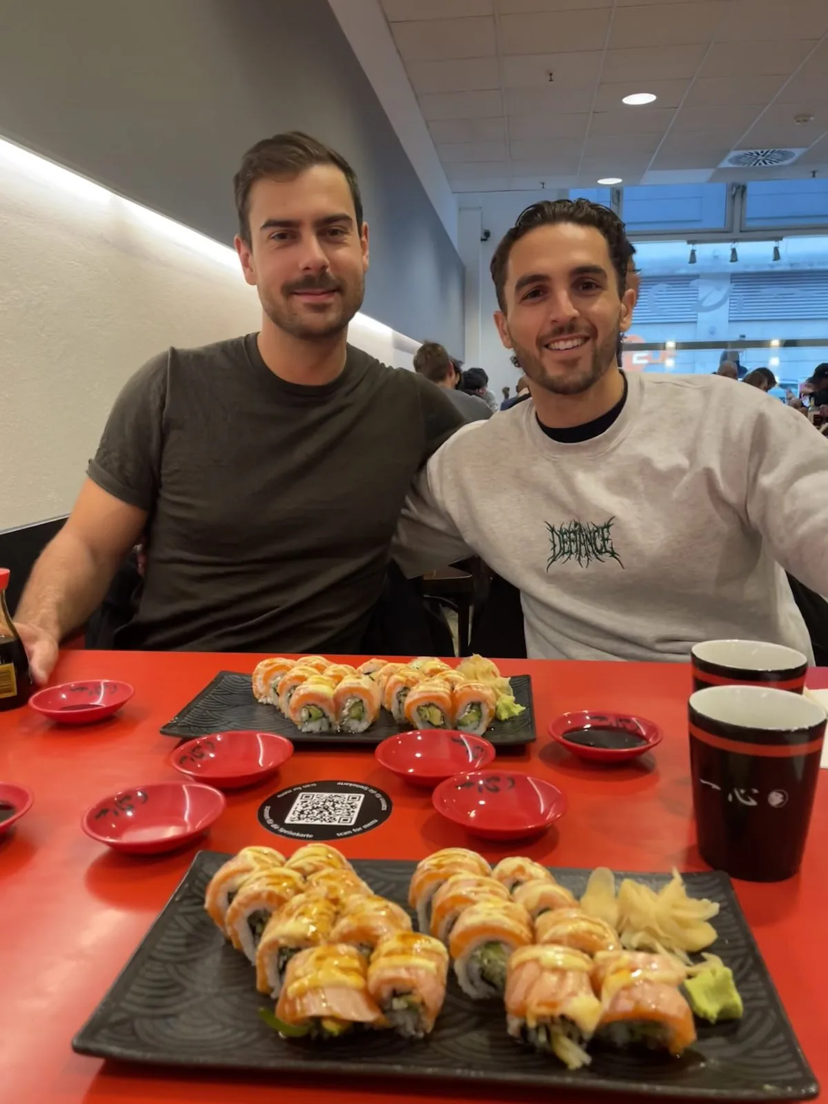 Mike McDonnell and Jacob of Active+ sharing sushi at a red-tabled restaurant